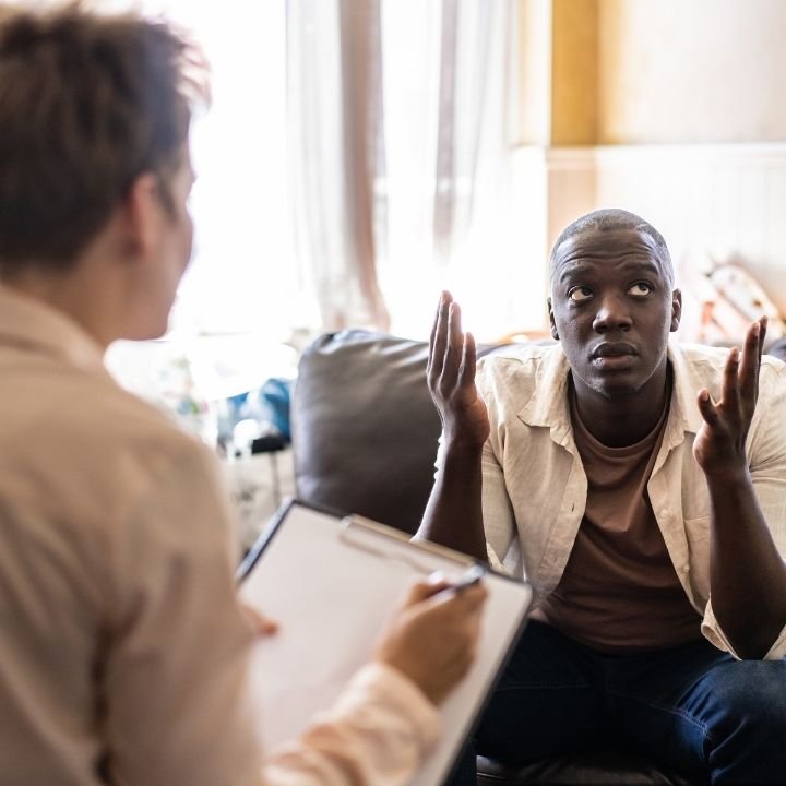 Client raising hands in confusion while discussing trauma with therapist