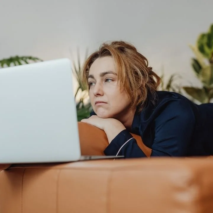 Woman lying on a couch staring at a laptop, showing signs of low energy and disengagement.