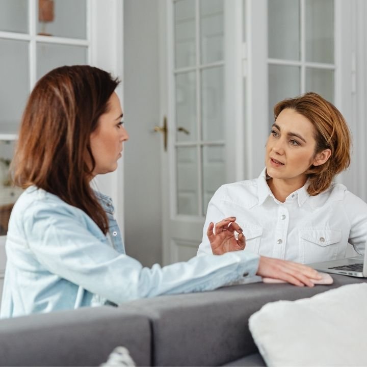 Female therapist and client sitting on a couch engaged in a serious conversation.