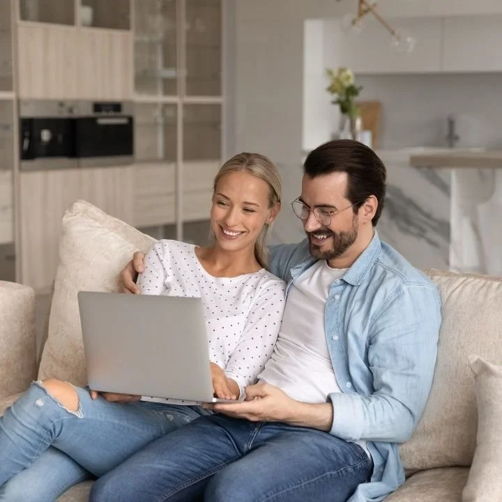Couple sitting together holding hands while looking at a laptop.