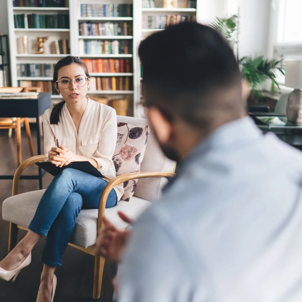 Therapist sitting with legs crossed listening intently to a male client during a counseling session