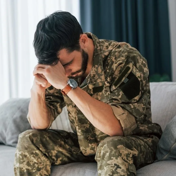 Soldier in camouflage uniform sitting on couch with head bowed