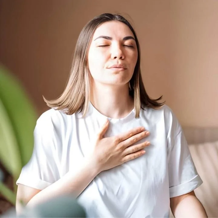 Woman practicing grounding breathing technique with hand on chest to reduce panic symptoms.
