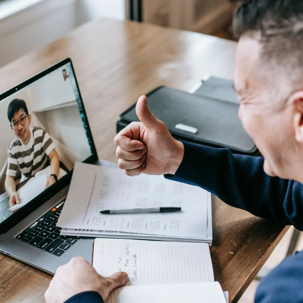 Smiling man giving a thumbs-up during a virtual therapy session with therapist visible on laptop screen