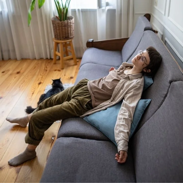 Person lying flat on a sofa with arms relaxed, appearing emotionally drained in a quiet living room.