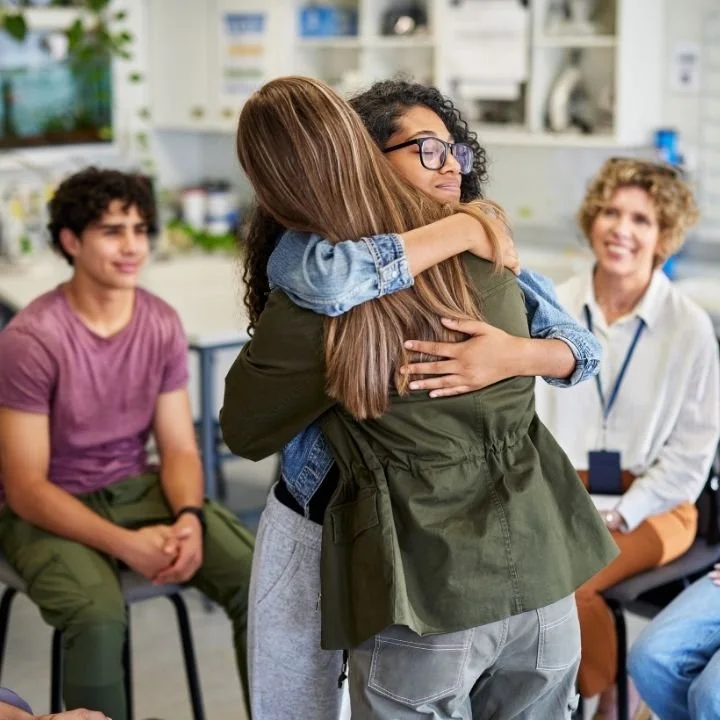 Two people hugging during a group support session while others look on.