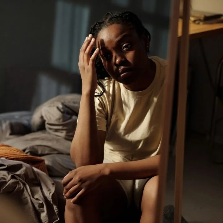 Woman sitting on bed holding her head with tired expression
