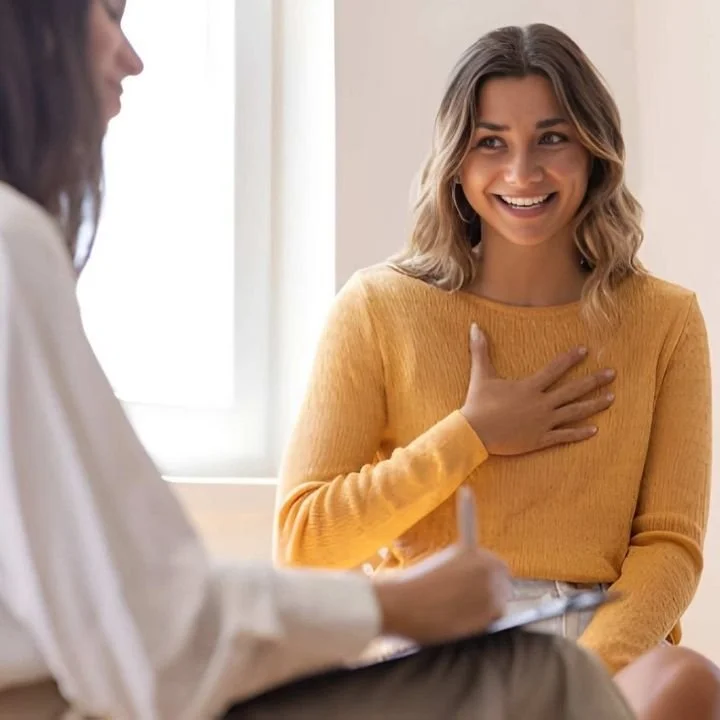 Client smiling and placing hand on chest while speaking during therapy session.