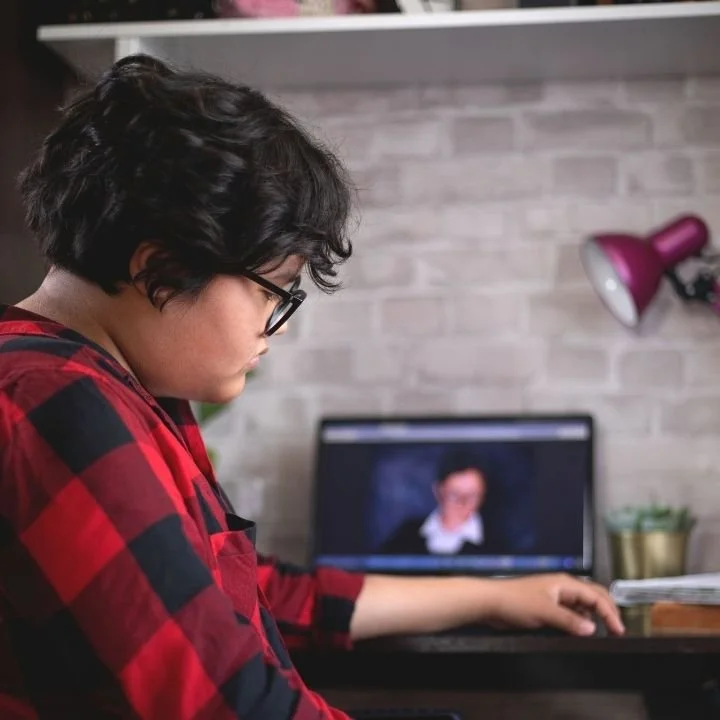 Person in red plaid shirt sitting at desk, looking down sadly