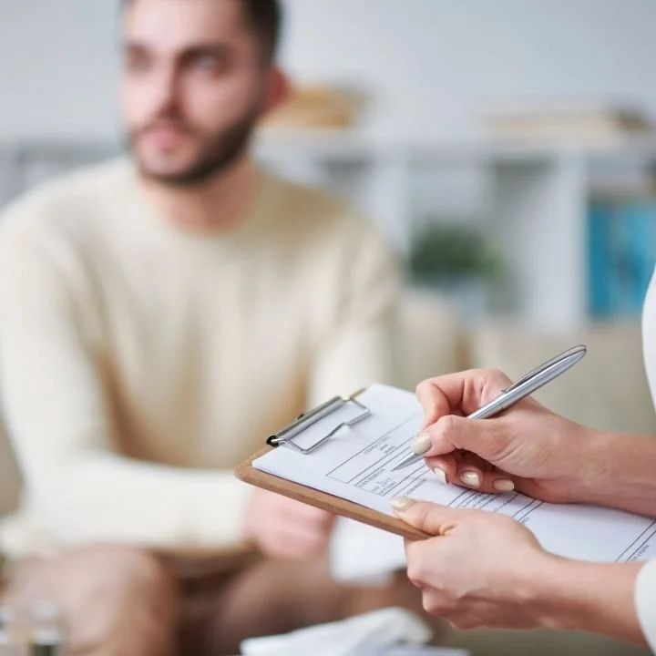 Therapist writing notes on clipboard during counseling with male client