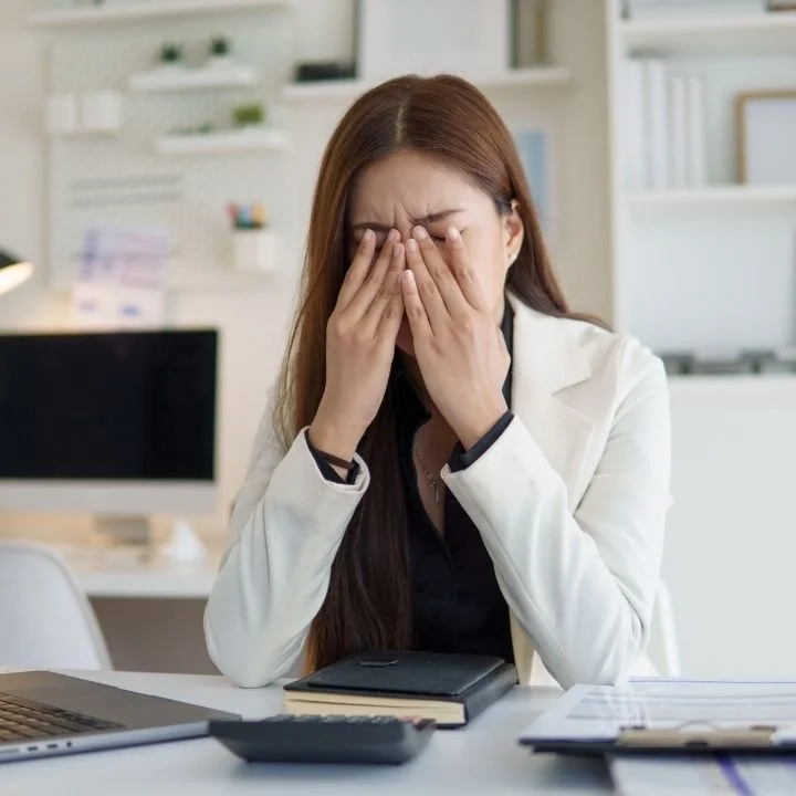 Woman sitting at desk in office, covering face with both hands