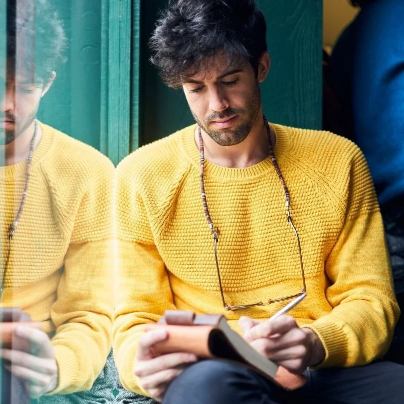 Man in yellow sweater writing in journal as part of anxiety coping practice.