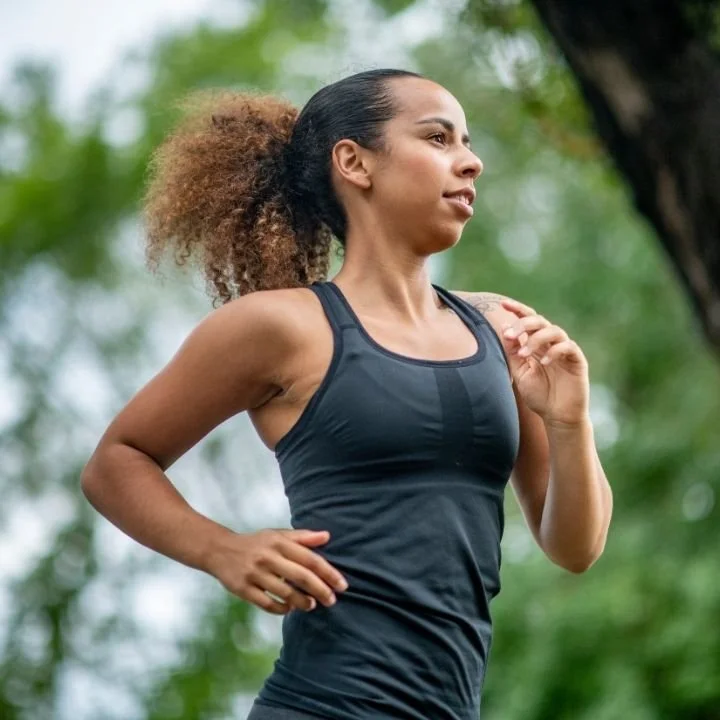Woman jogging outdoors in a park, engaging in physical activity to regain energy.