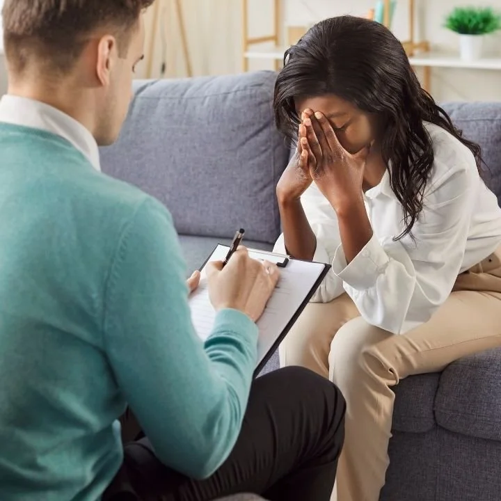 Woman covering face in therapy session while counselor takes notes