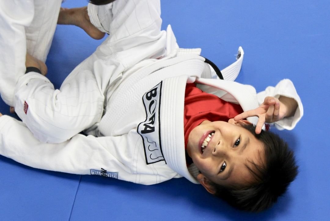 A child smiling while practicing Jiu-Jitsu on the mats