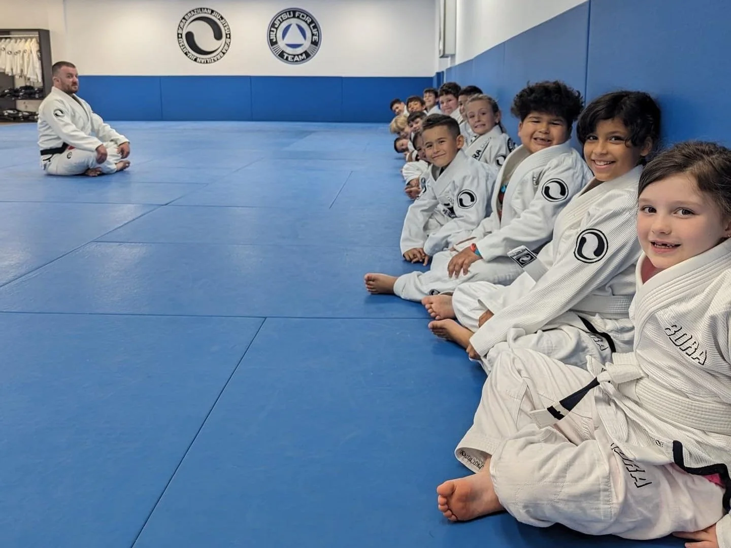 Children sitting together along the edge of the Bora mats