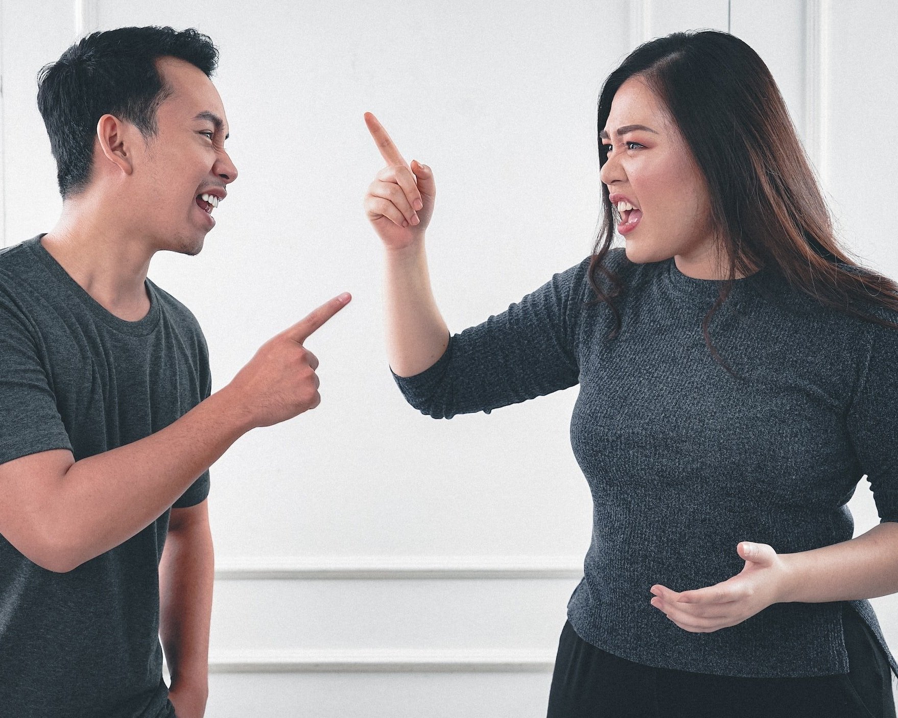 A man and am woman representing a couple, are in a heated argument with scowling expressions and pointing fingers. This image represents criticism as one of the 4 horsemen and warning signs of divorce.
