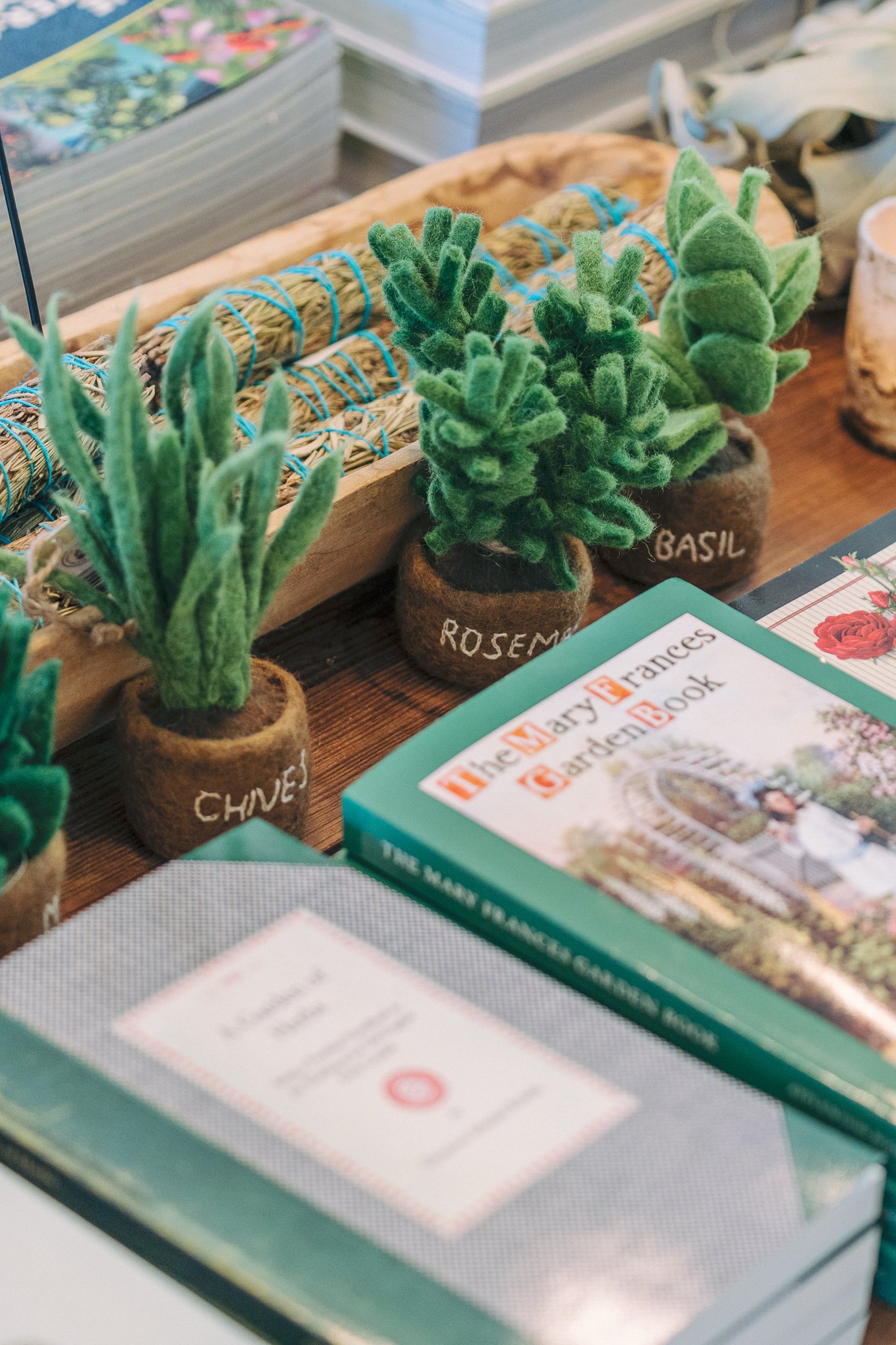Felt herb decorations with "Chives," "Rosemary," and "Basil" labels, surrounded by gardening books, including 'The Mary Frances Garden Book'.
