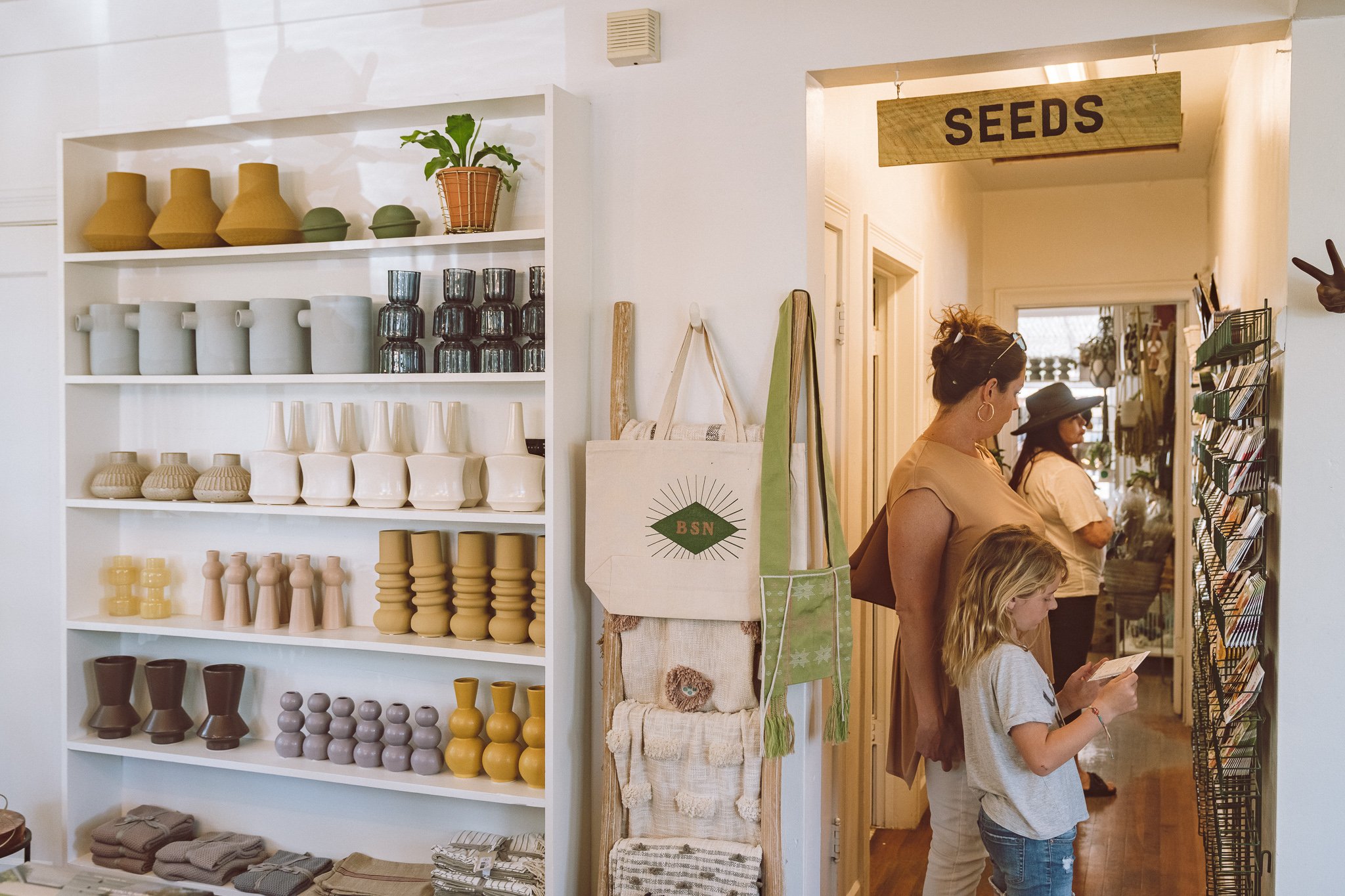 Shop interior with pottery, towels, bags, and people browsing seed packets.