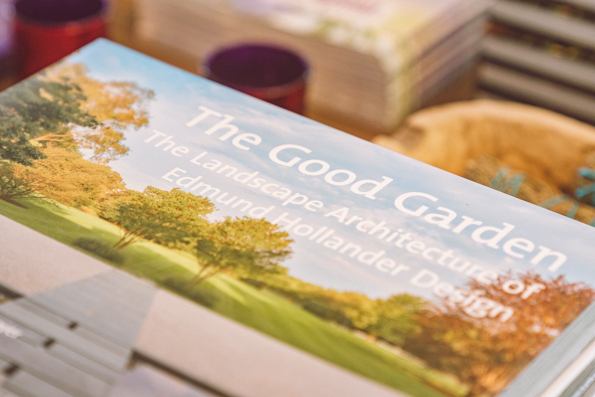 Close-up of a book titled 'The Good Garden: The Landscape Architecture of Edmund Hollander Design' with a nature scene on the cover.