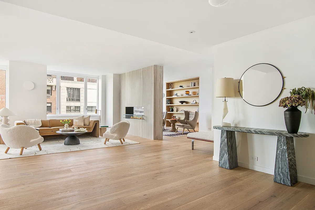 Modern living room with large windows, light-colored furniture, and wooden flooring.