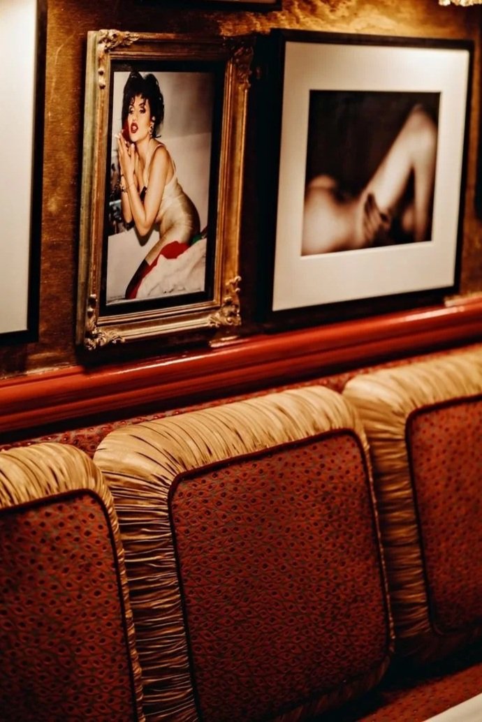 Framed photographs on a wood-paneled wall above a cushioned, patterned bench in a dimly lit interior space.