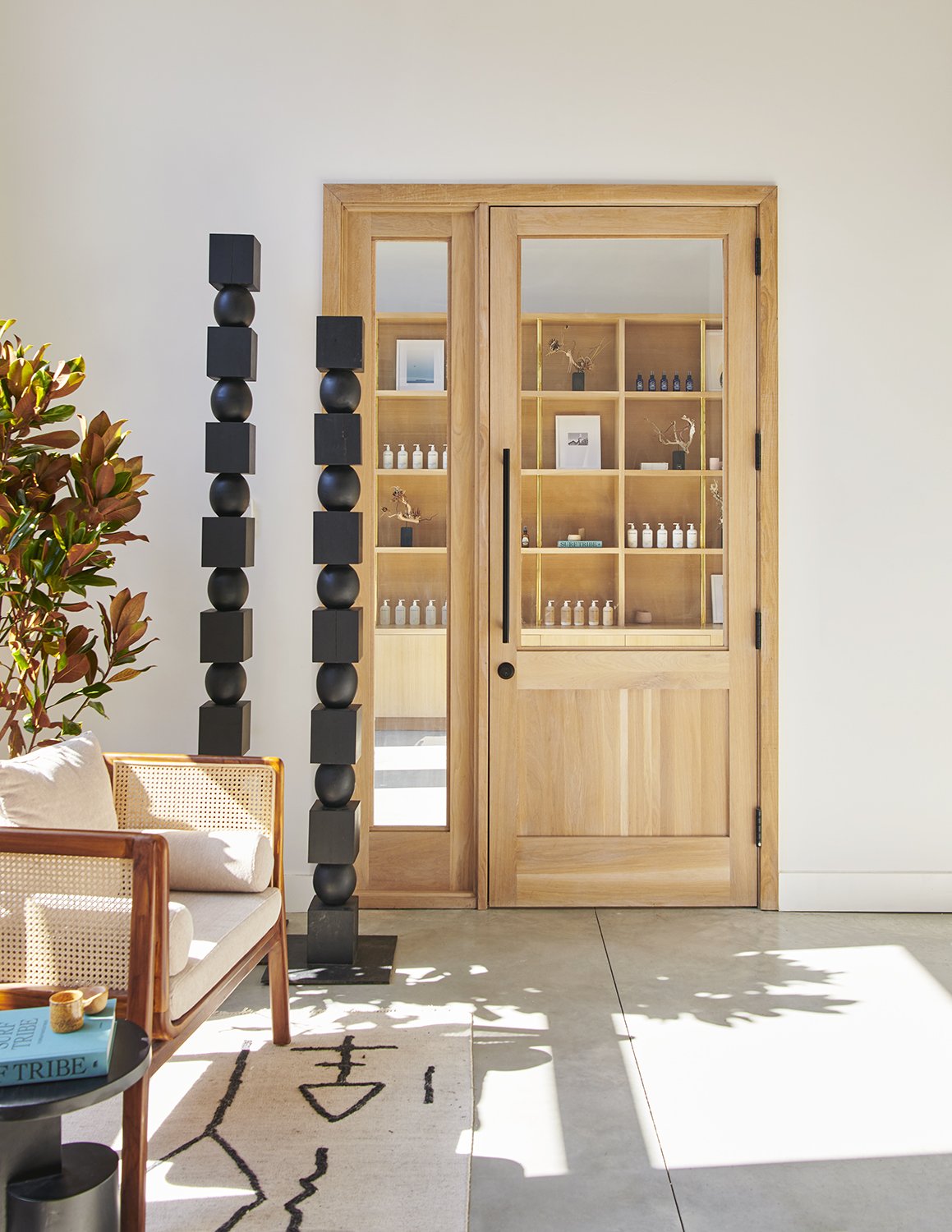 Modern living room with wooden sliding door, black decorative sculptures, beige sofa with wooden frame, and a black side table with a turquoise book, all illuminated by natural sunlight.