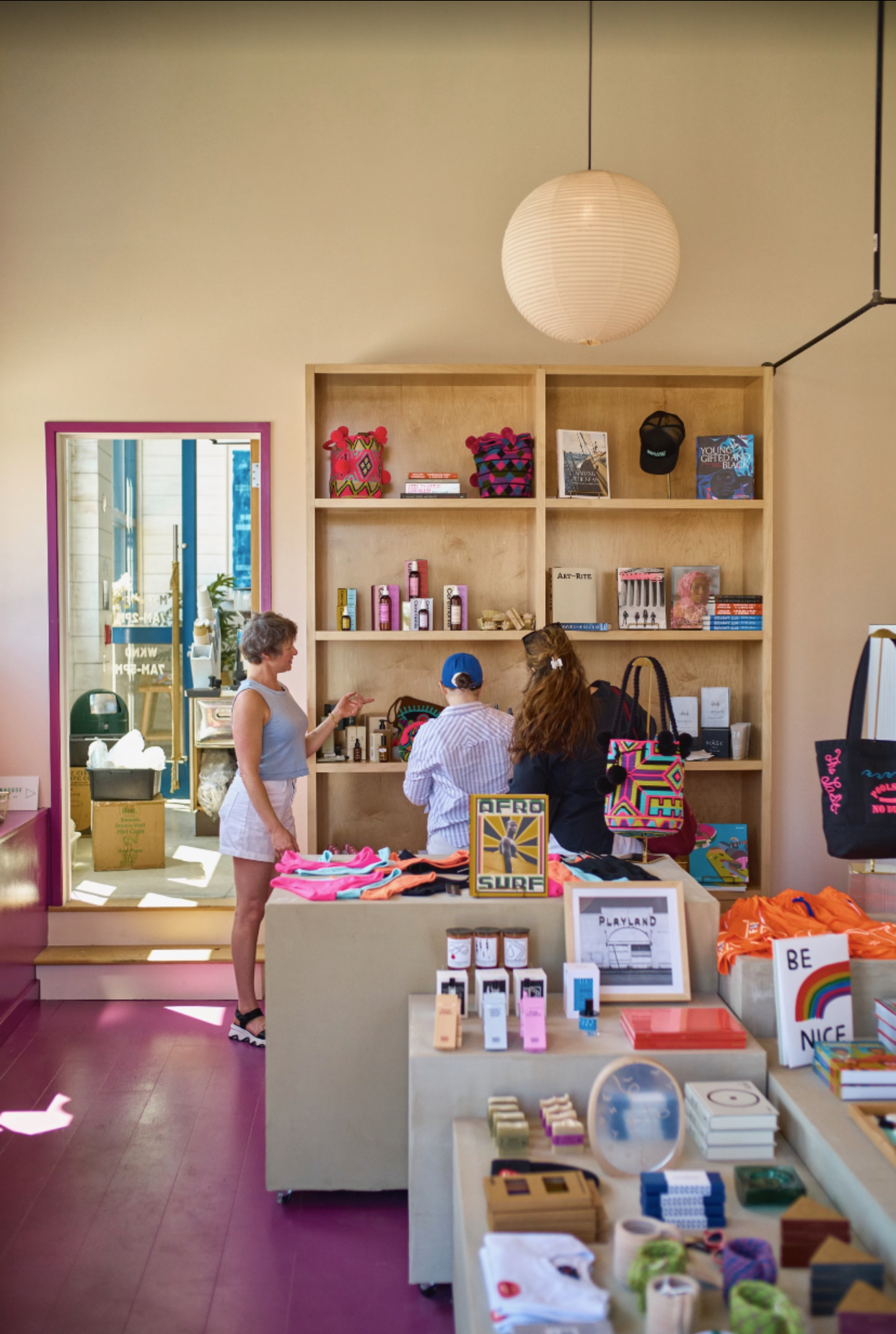 People shopping inside a brightly lit retail store with colorful merchandise, wooden shelves, and display tables.