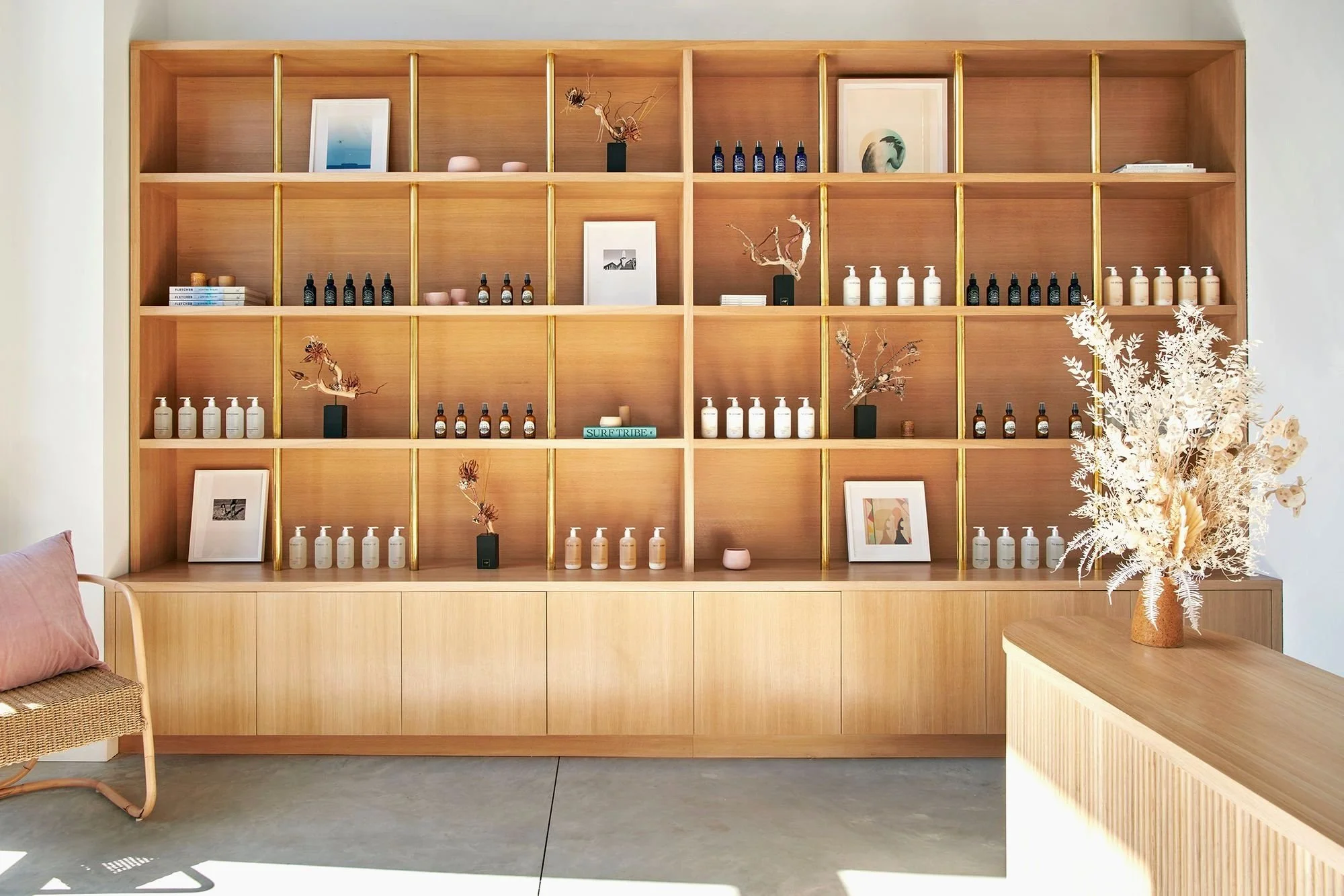 Wooden shelving unit with decorative items and bottles, framed art, dried floral arrangements, and a large bouquet on a wooden table to the right.