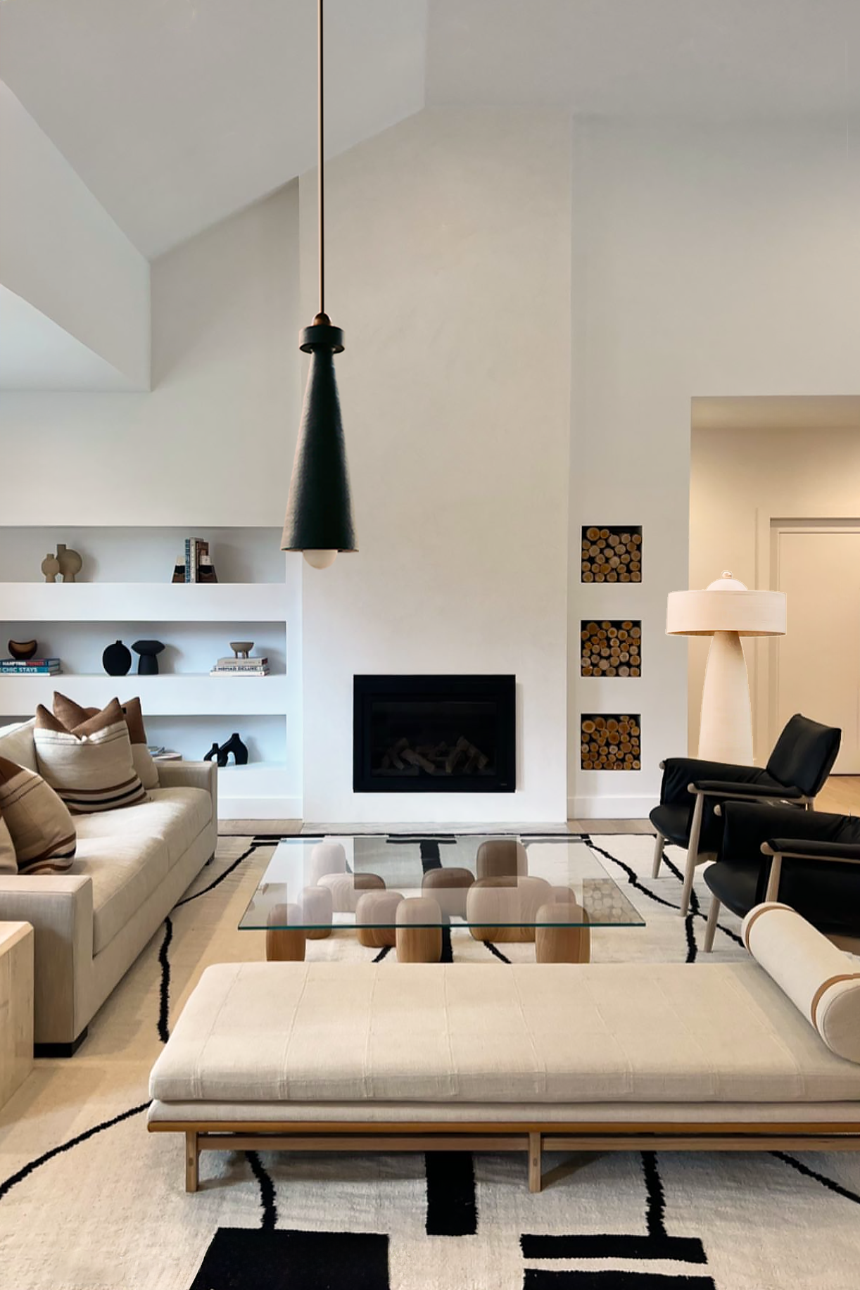 Modern living room with beige sofa, black armchairs, glass coffee table, fireplace, and built-in shelves, decorated with books and sculptures. Leaf-shaped lighting fixtures.
