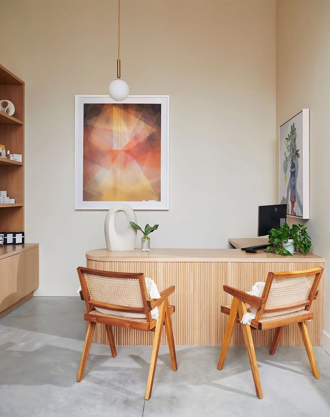 Rockaway Spa Interior Design. A modern office reception area with two wooden chairs, a wooden counter, a computer, and contemporary decorations including framed art and potted plants.