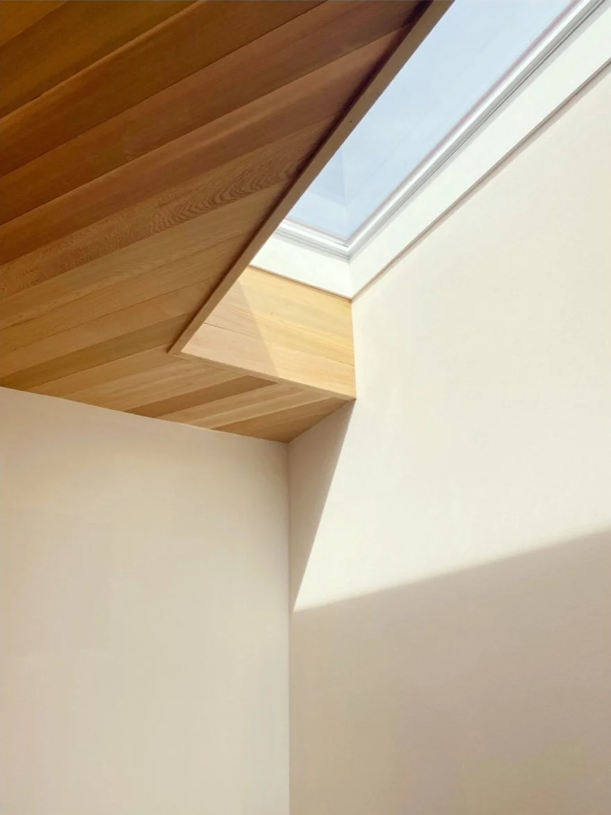 Close-up view of a rooftop corner with wooden paneling and a skylight window, showing a white wall and ceiling.