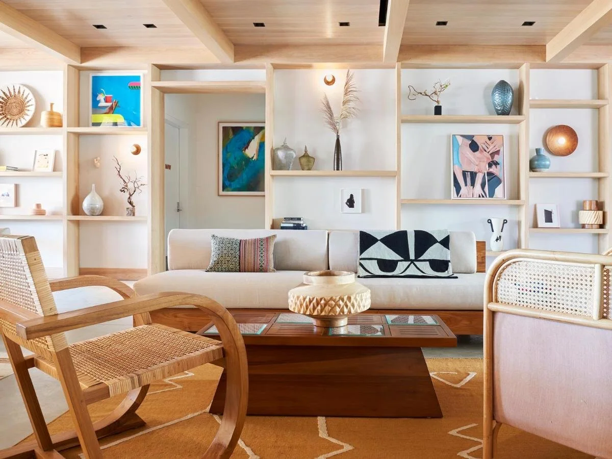Living room with white sofa, wooden chairs, a wooden coffee table, and decorative items on shelves, including vases and artwork, in a modern, minimalistic style.