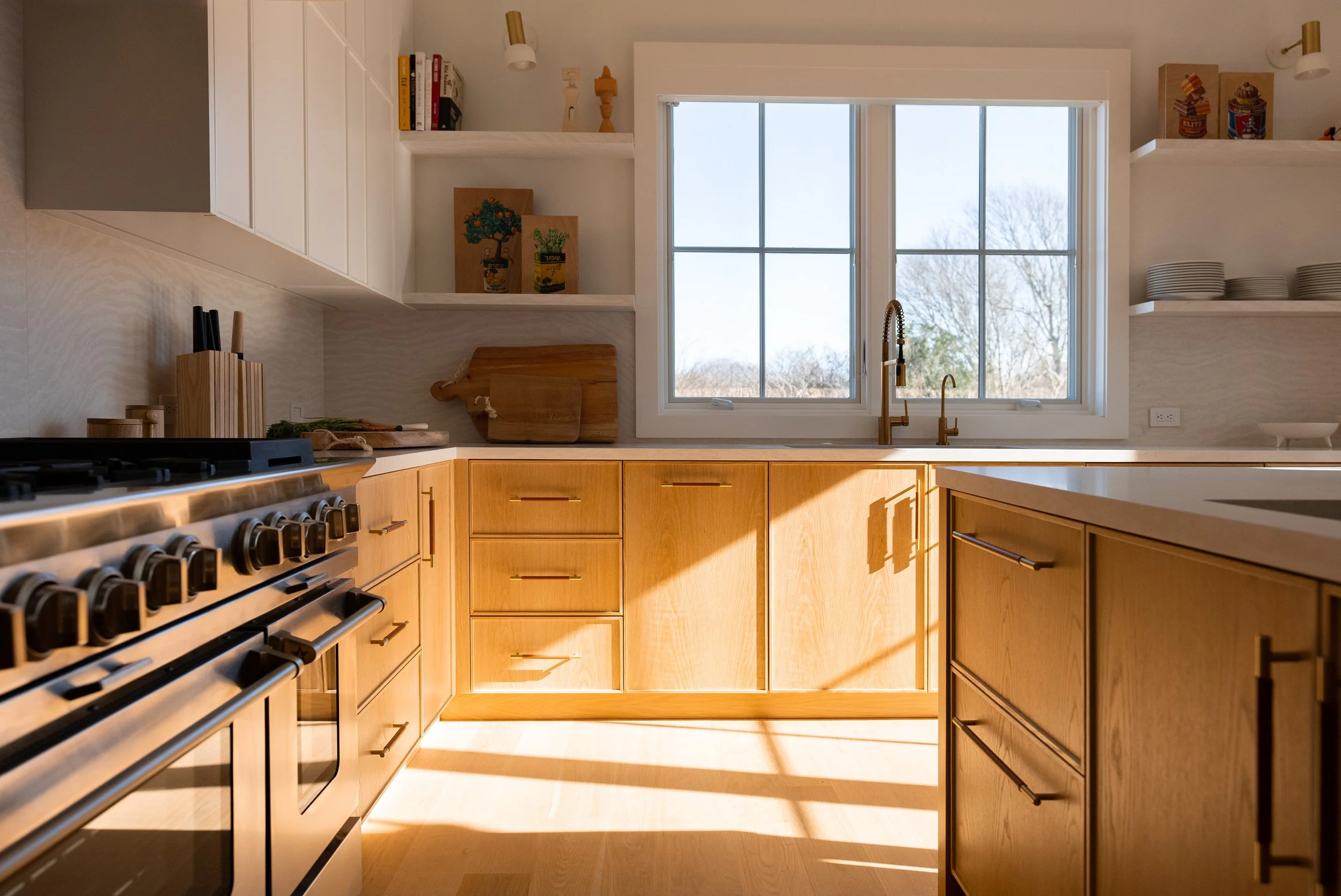 Sunlit kitchen with wooden cabinets, white countertops, a window, and open shelves with dishes and decor.