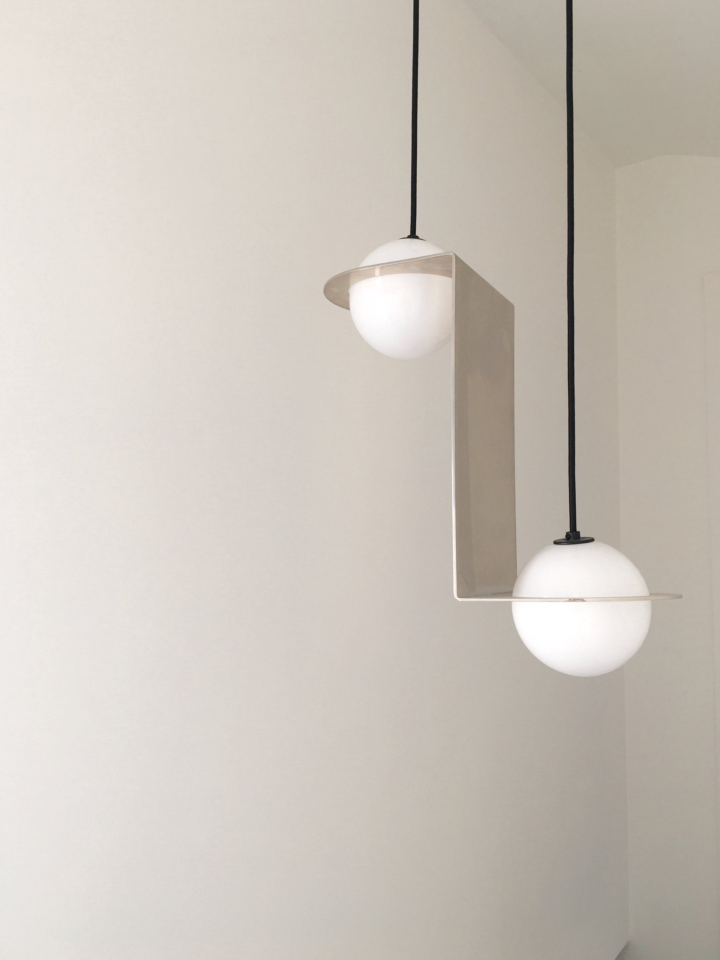 Los Angeles interior Design. Modern white pendant light fixture with two spherical globes hanging from black cords against a plain white wall.