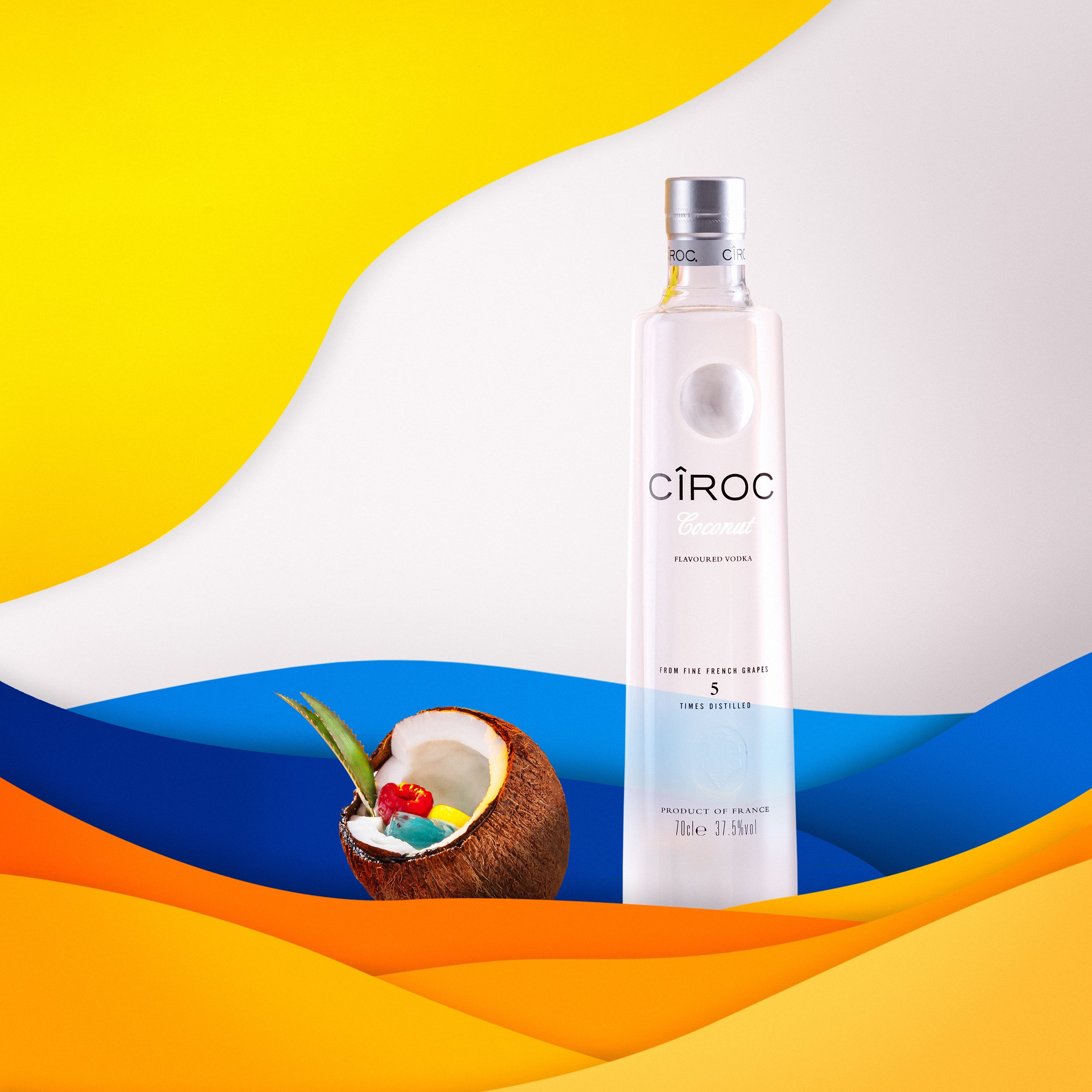 Bouteille de vodka Cîroc Coconut et demi-noix de coco avec bonbons, sur fond coloré jaune et bleu.