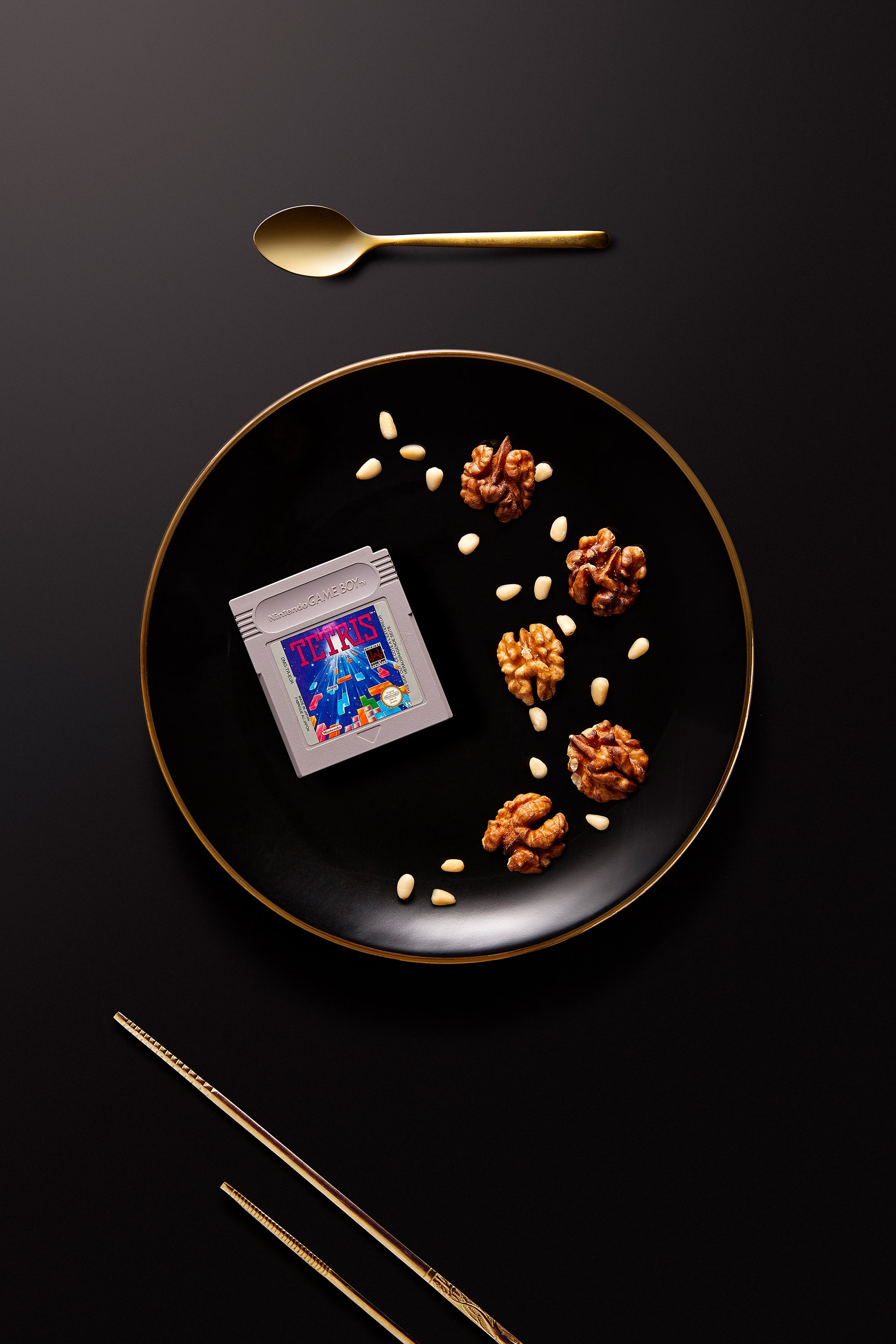 Cartouche de jeu sur une assiette avec des noix et des pignons, cuillère dorée et baguettes à proximité.