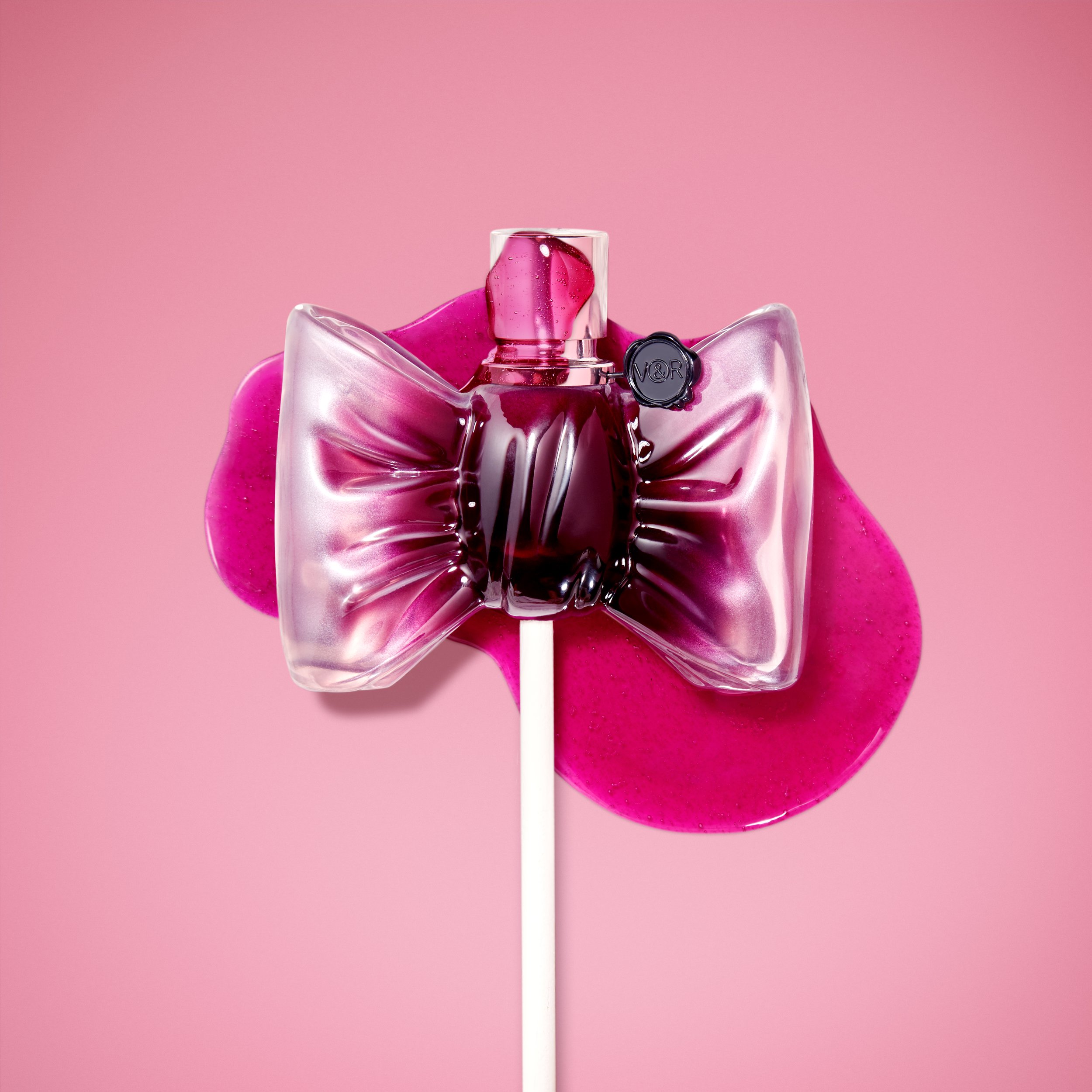 Bouteille de parfum en forme de nœud sur fond rose.
