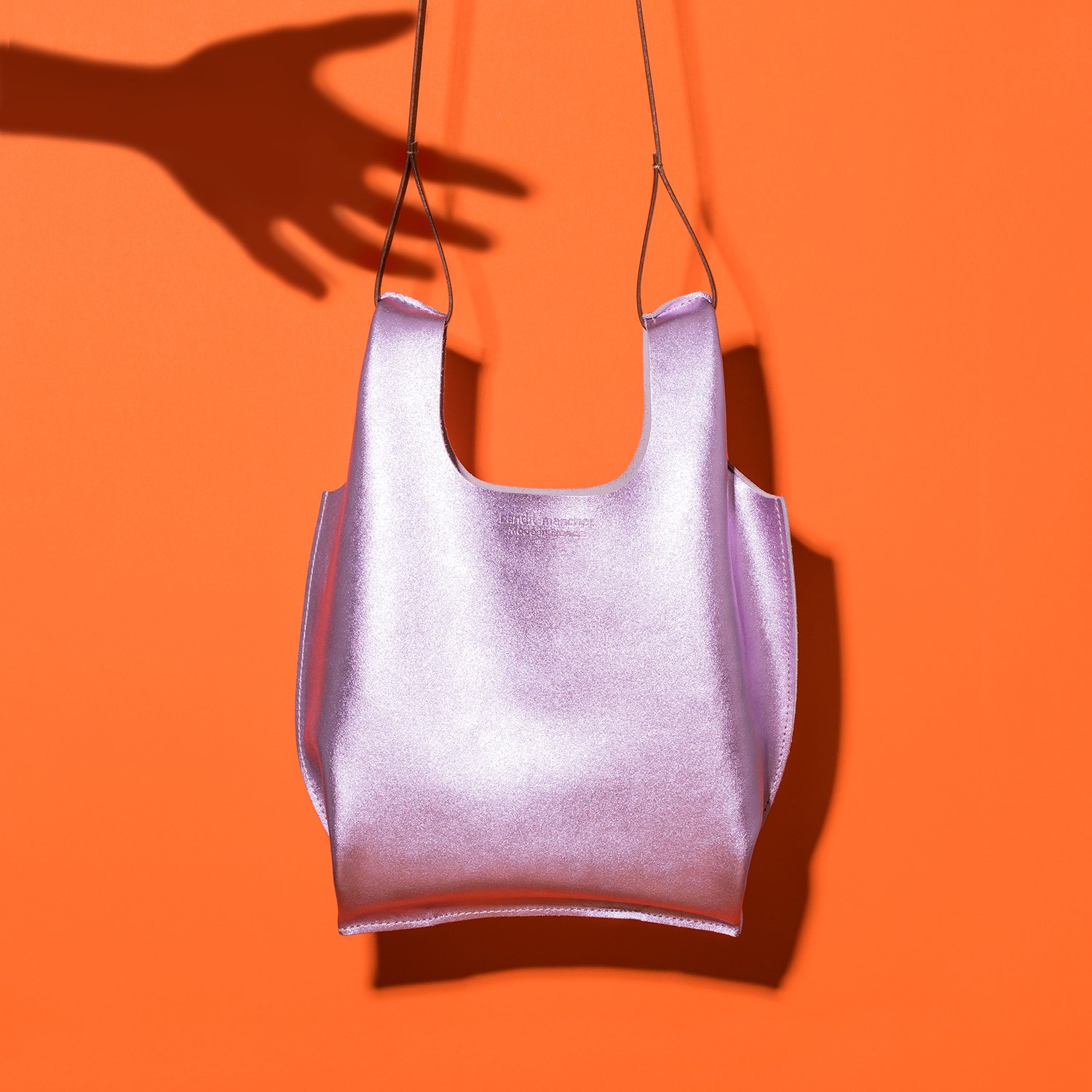 Sac à main violet avec une ombre de main, sur fond orange vif.