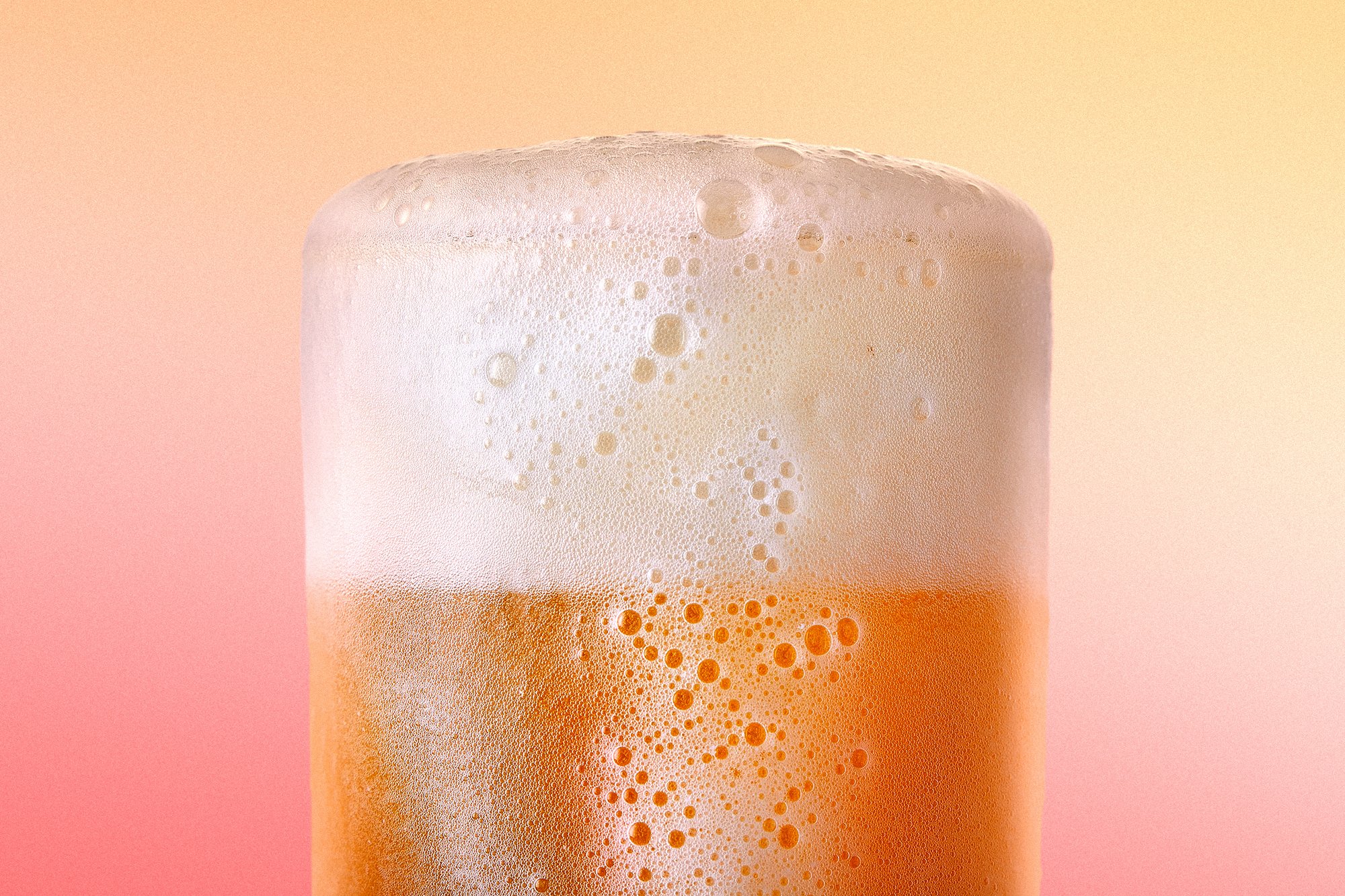 Verre de bière avec mousse sur un fond dégradé orange et rose.