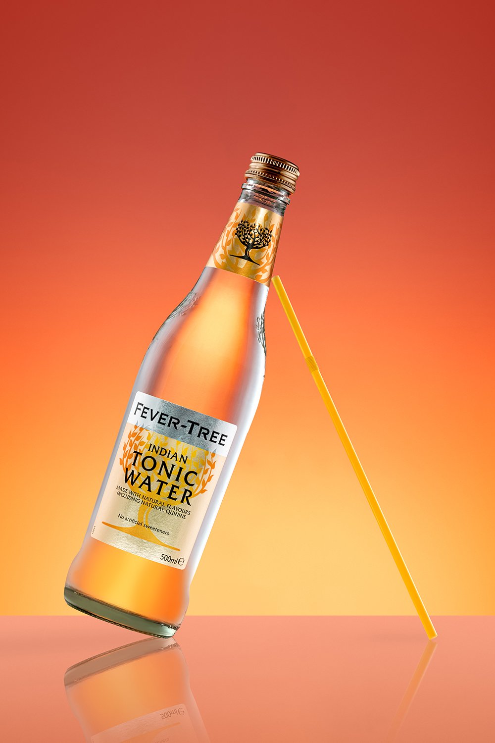 Bouteille de tonic Fever-Tree Indian sur fond dégradé orange avec une paille jaune.