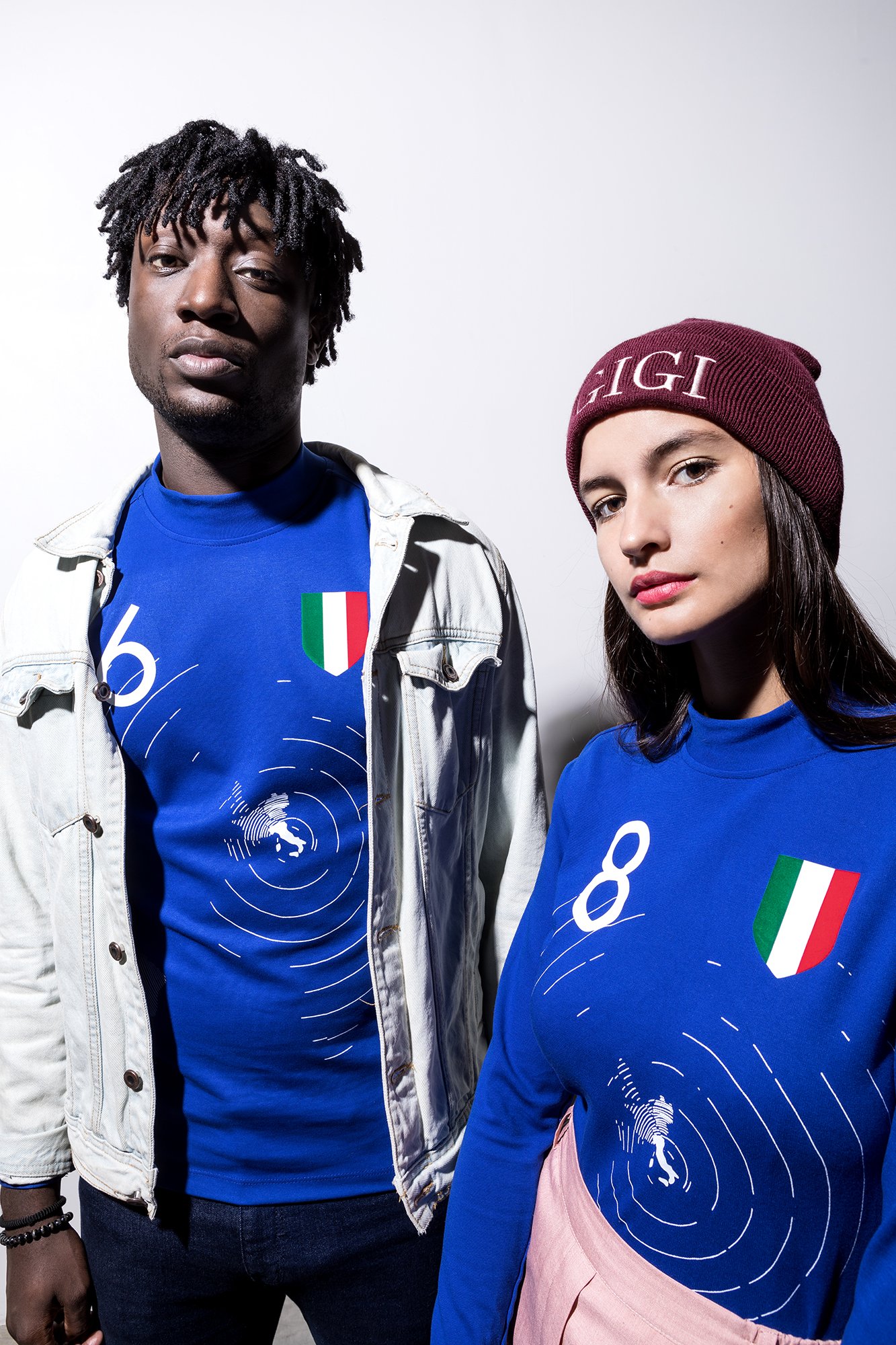 Deux personnes portant des t-shirts bleus avec un drapeau italien, l'une avec une veste en jean et l'autre avec un bonnet rouge portant l'inscription "GIGI".