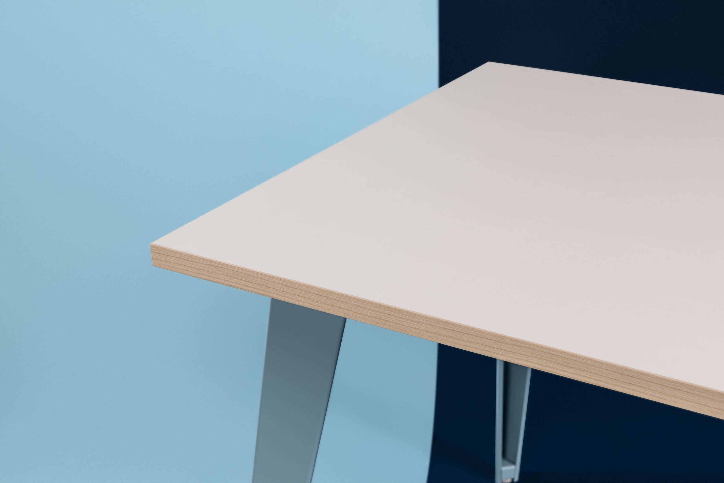 Coin d'une table avec plateaux blancs et pieds métalliques, fond bleu et noir.