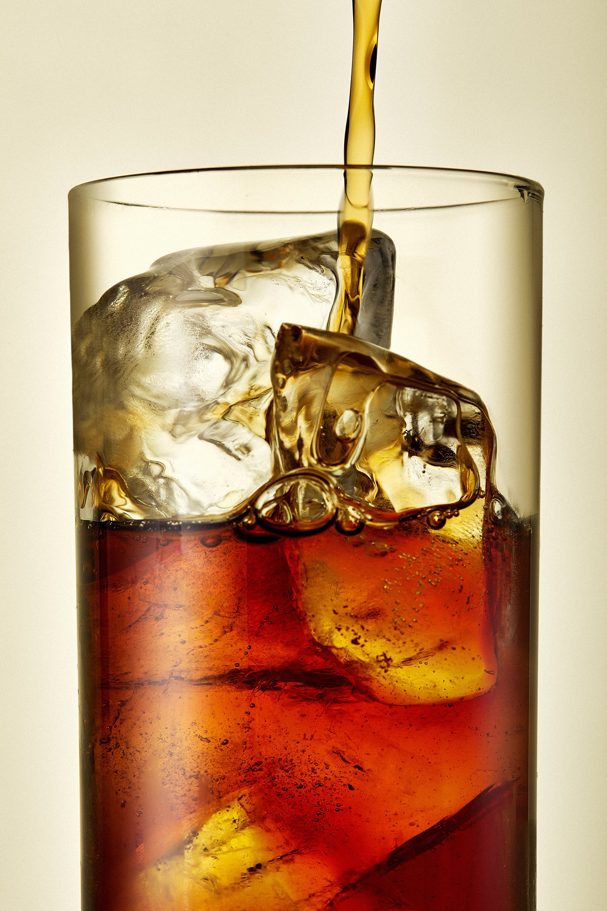 Un verre de soda avec des glaçons, liquide brun en train d'être versé.