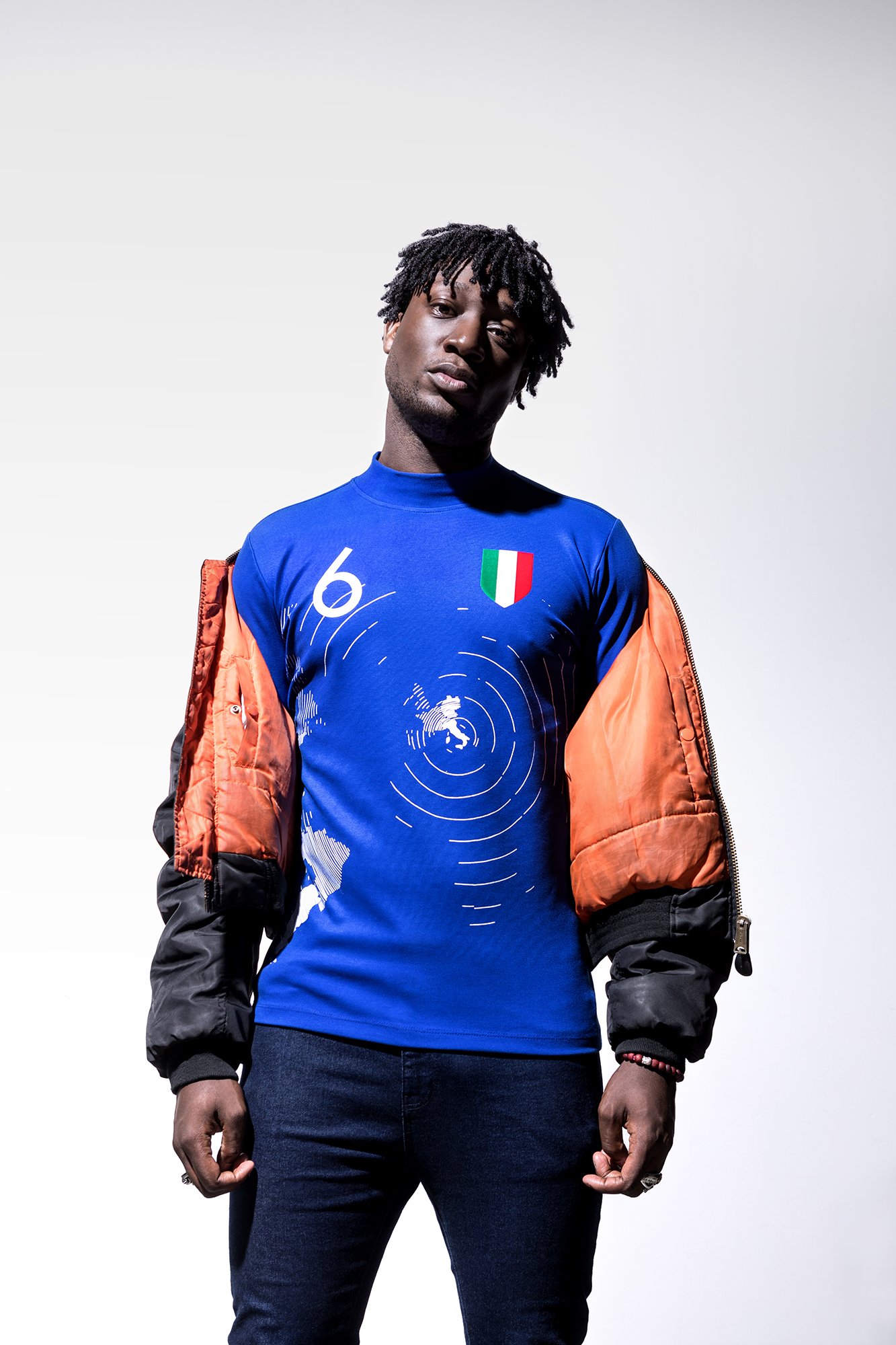 Homme portant un maillot bleu avec des motifs et un drapeau italien, et une veste en partie ouverte.