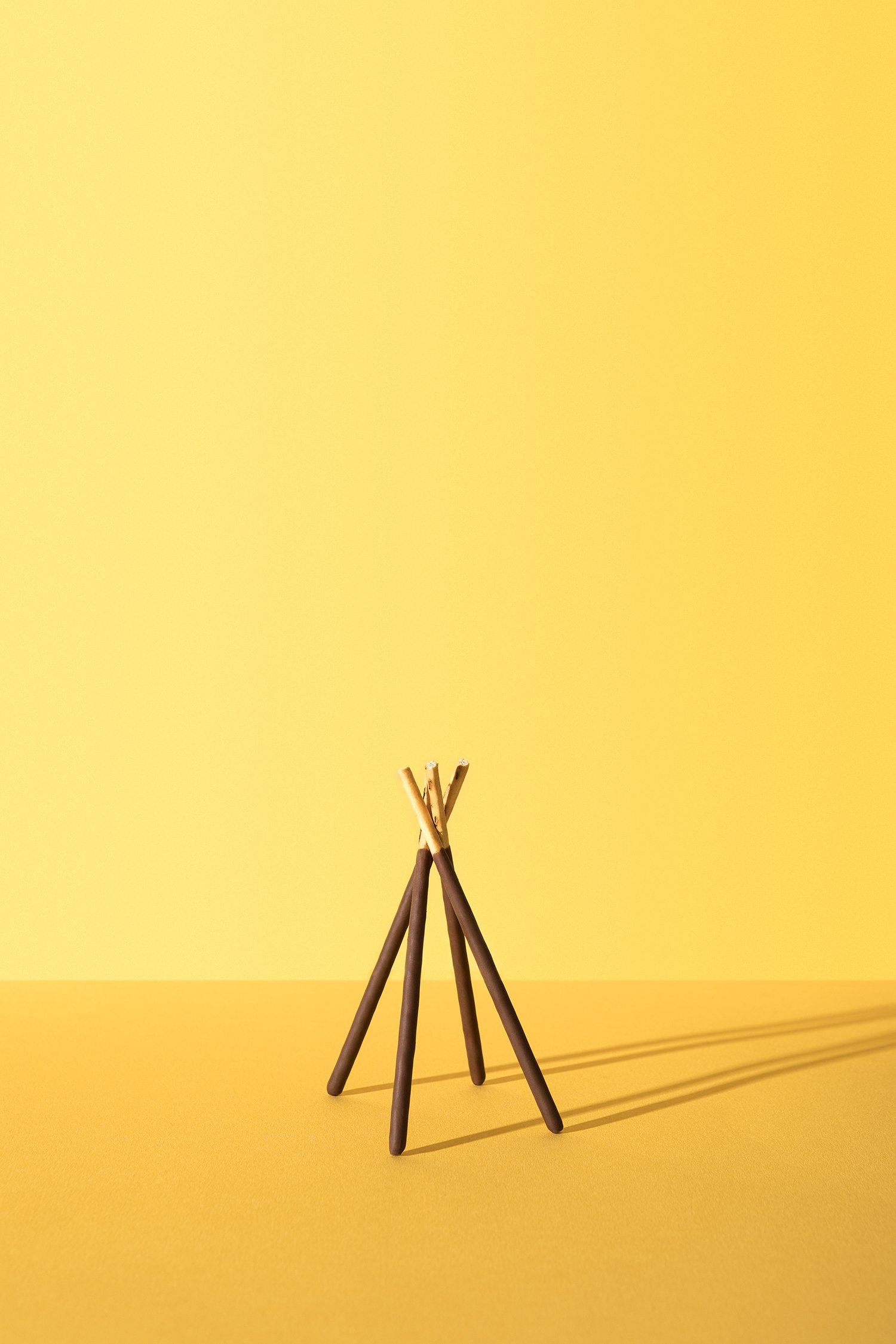 Des biscuits en bâtonnets recouverts de chocolat disposés en forme de tipi sur un fond jaune.