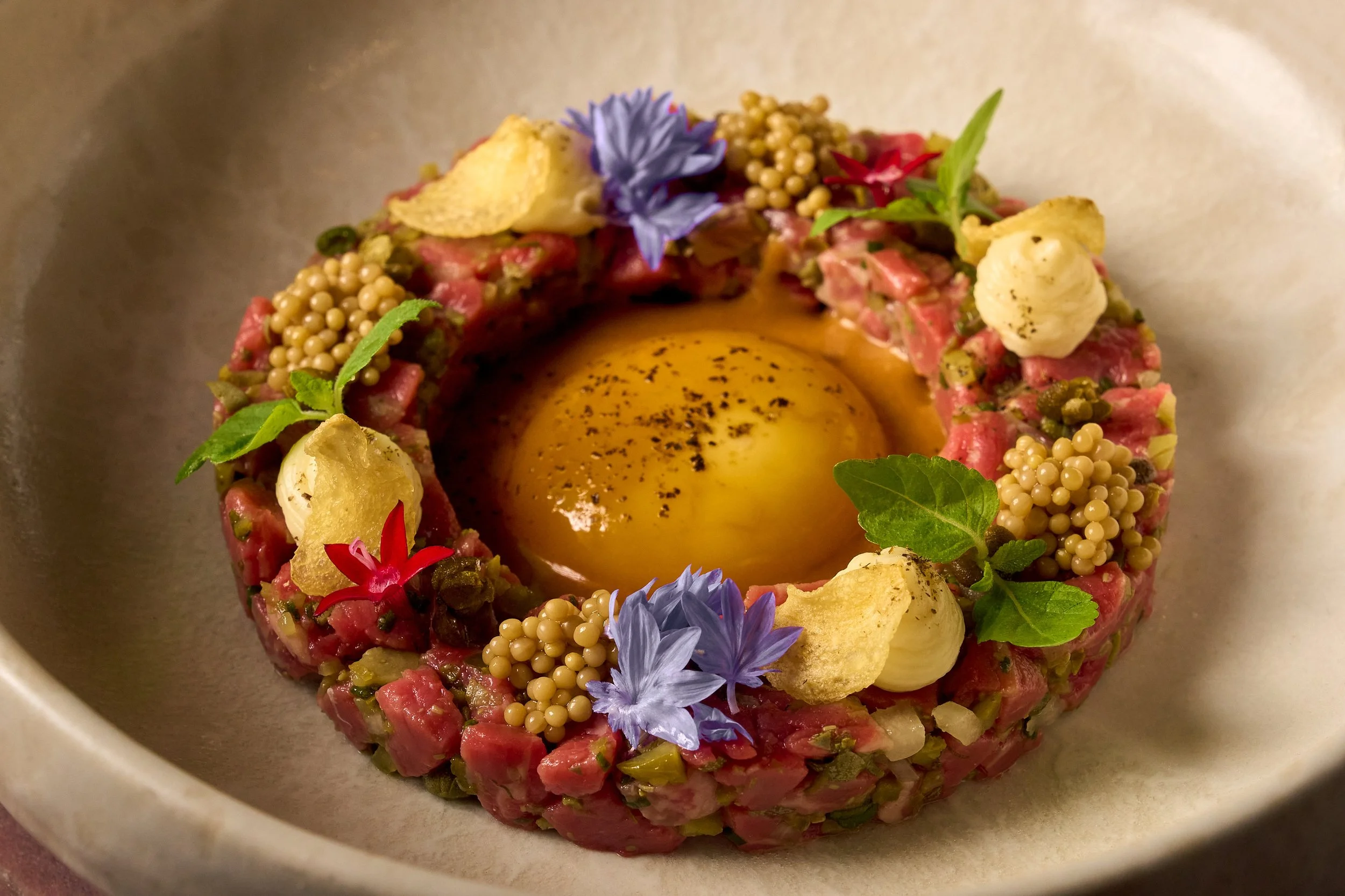 MILA's iconic beef tartare, with a raw egg in the center and the beef tartare garnished with edible flowers and leaves.