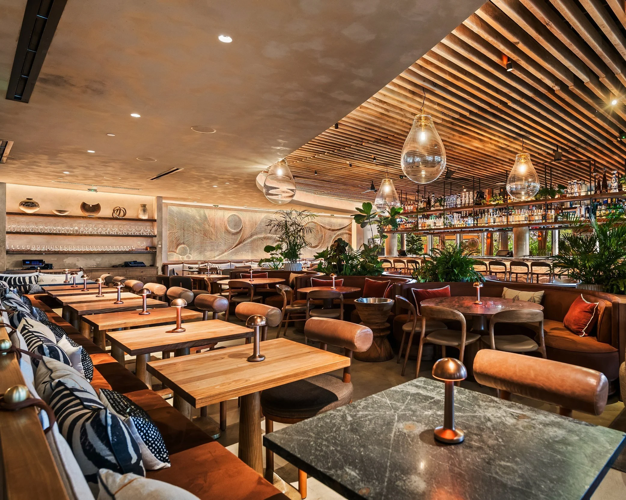 interior view of MILA with rectangle small tables on the bottom right and round tables top center. The atmosphere is vibrant and refined.