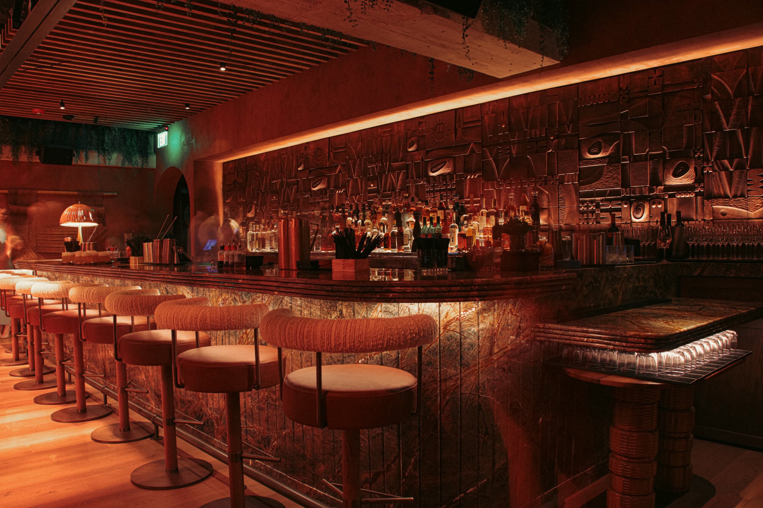 Red lighting and a luxurious setting of MILA Lounge bar with chairs lining the bar counter