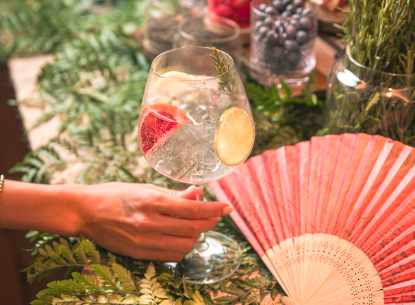 A refreshing brunch cocktail in a glass and garnishes, with a pink fan in the background